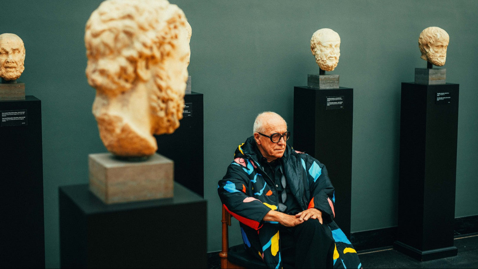 Ditlev Tamm sitting in a chair surrounded by classical sculpture heads in Ny Carlsbrg Glyptotek Copenhagen.